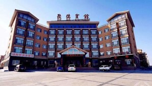 Un hotel de varios pisos con una entrada destacada y varios coches estacionados frente a él.