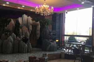 A restaurant interior with a rock formation backdrop, a chandelier, and outdoor seating visible through large windows.