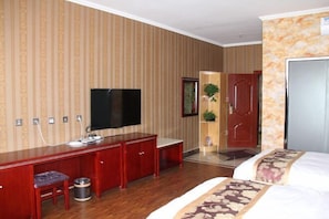 Une chambre d’hôtel avec un bureau en bois, une télévision, un lit avec une literie à motifs floraux et un miroir.