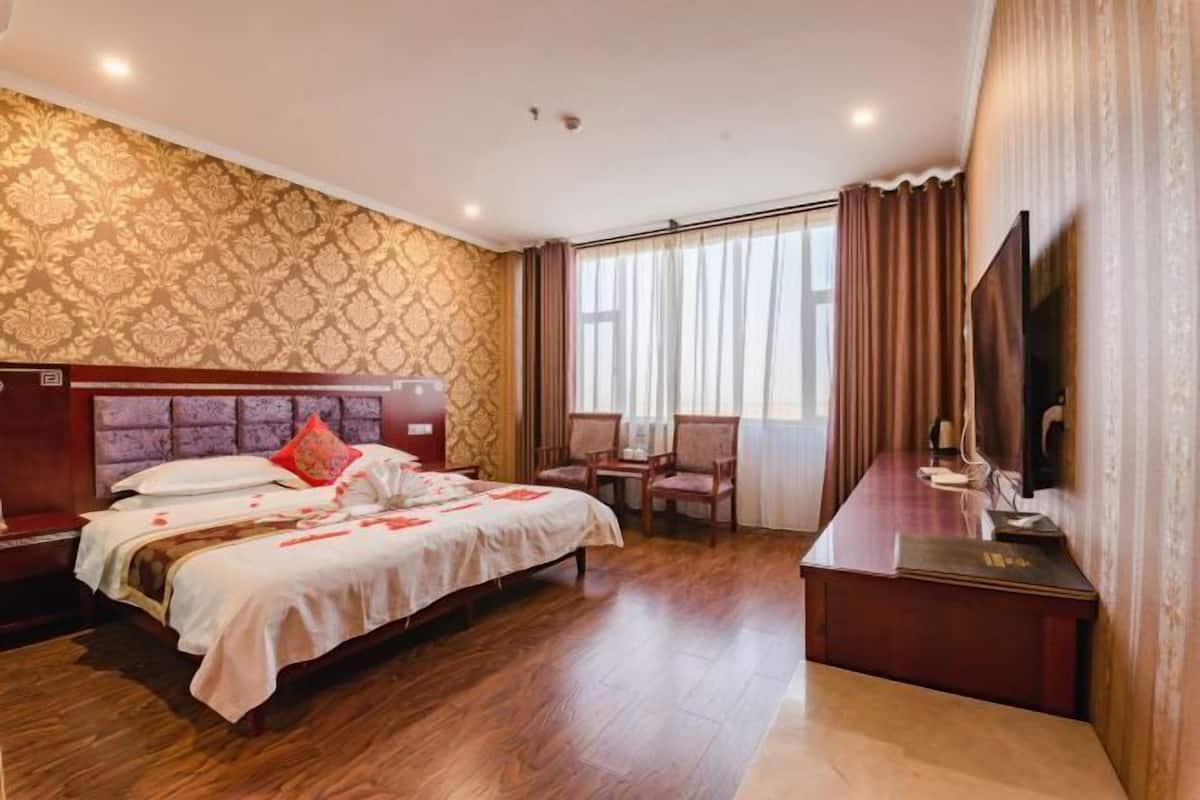 A hotel room with a large bed, a desk, a TV, and a window with curtains.