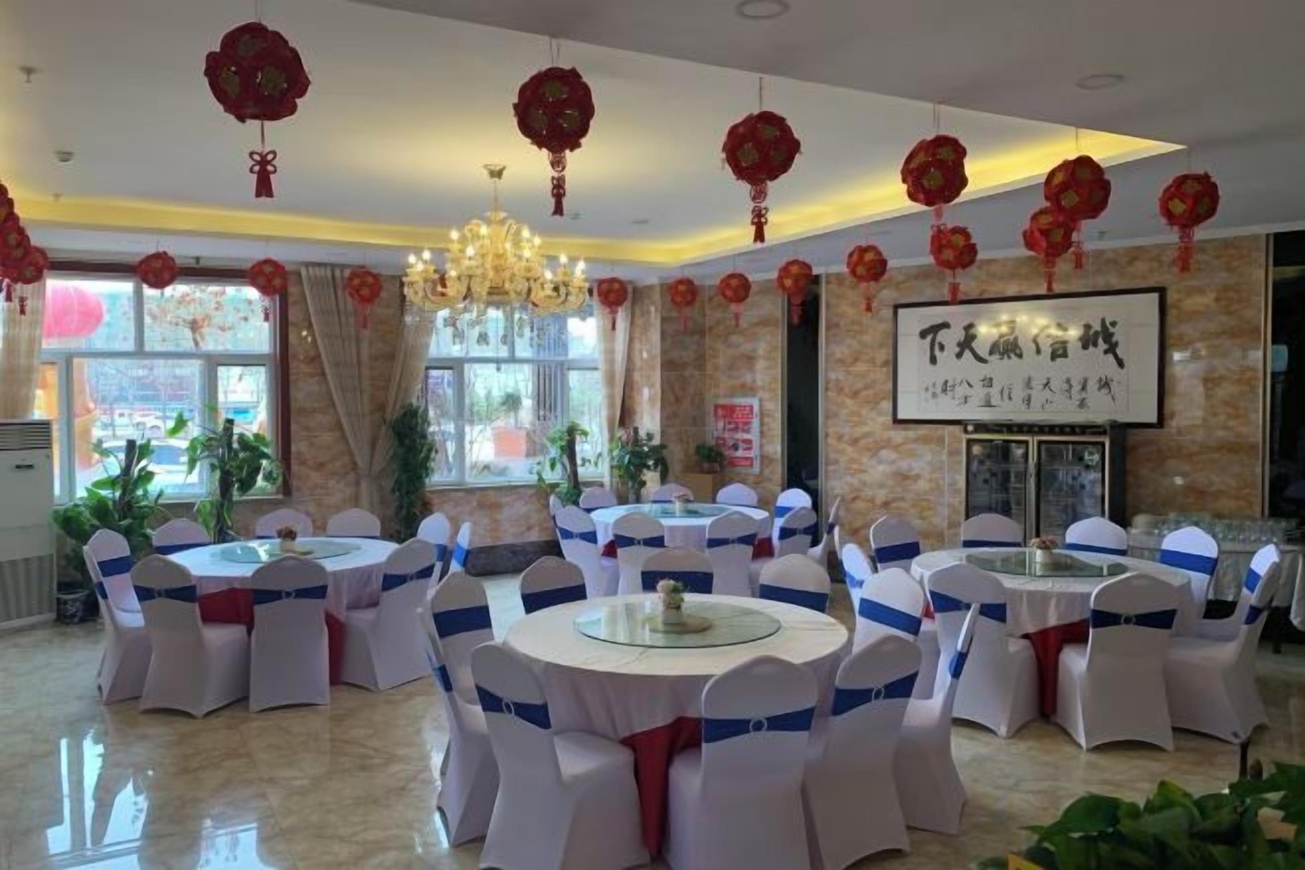 A banquet hall with round tables, white chairs, and red decorations.