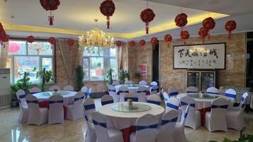 A banquet hall with round tables, white chairs, and red decorations.