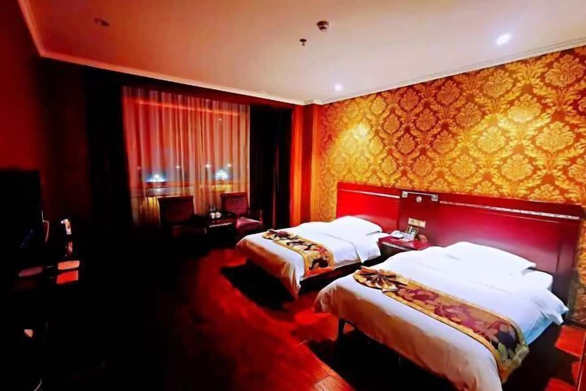 A hotel room with two beds, a large window with curtains, and a patterned wall.