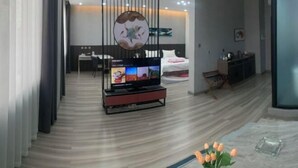 A modern hotel room with a TV, a bed, a desk, and a decorative wall panel. - Ju De Hotel (Jiayuguan)