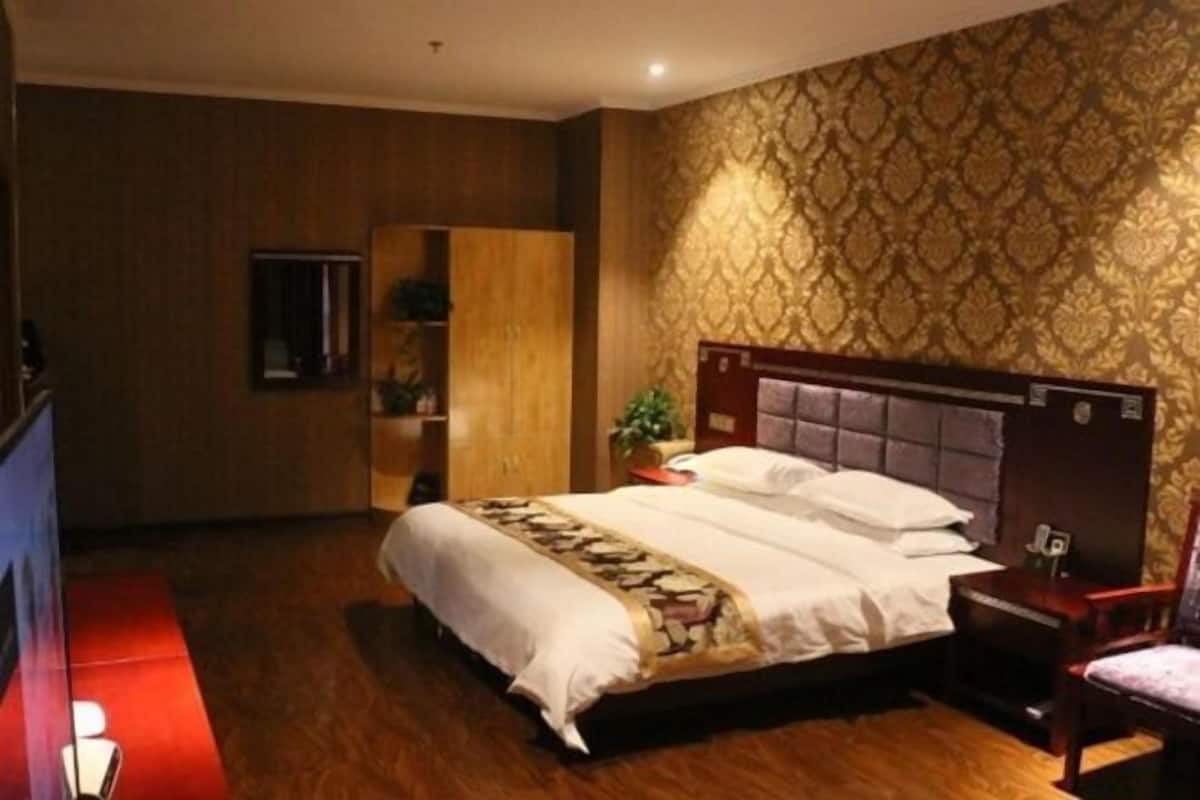 A hotel room with a bed, a wooden wardrobe, a small table, and a chair.