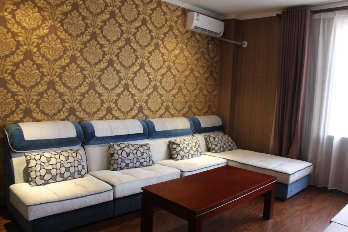 A living room with a sofa set, a wooden coffee table, and a patterned wallpaper.