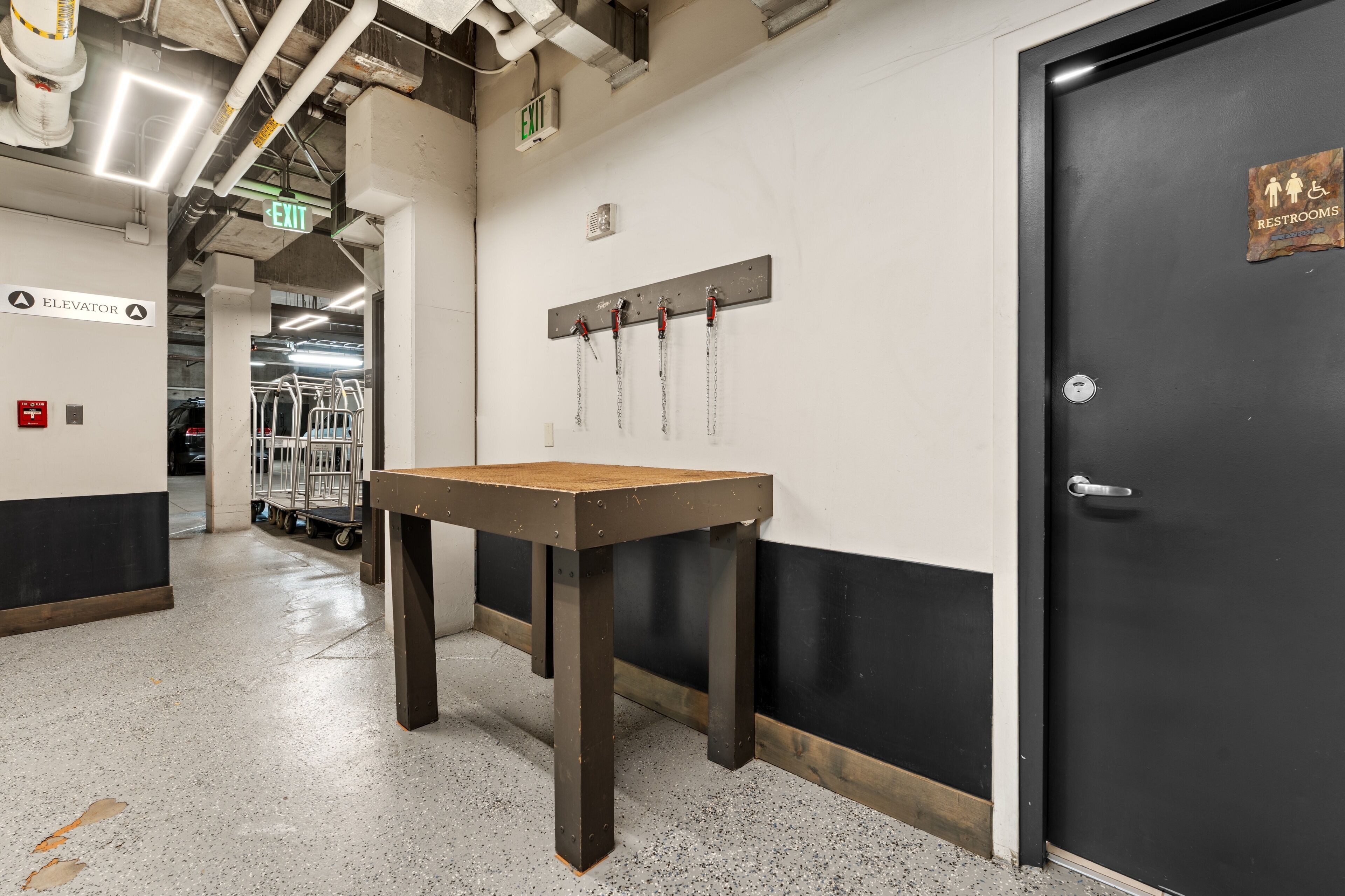 A hallway with an elevator sign, a table with a chain, and a door with a restroom sign.