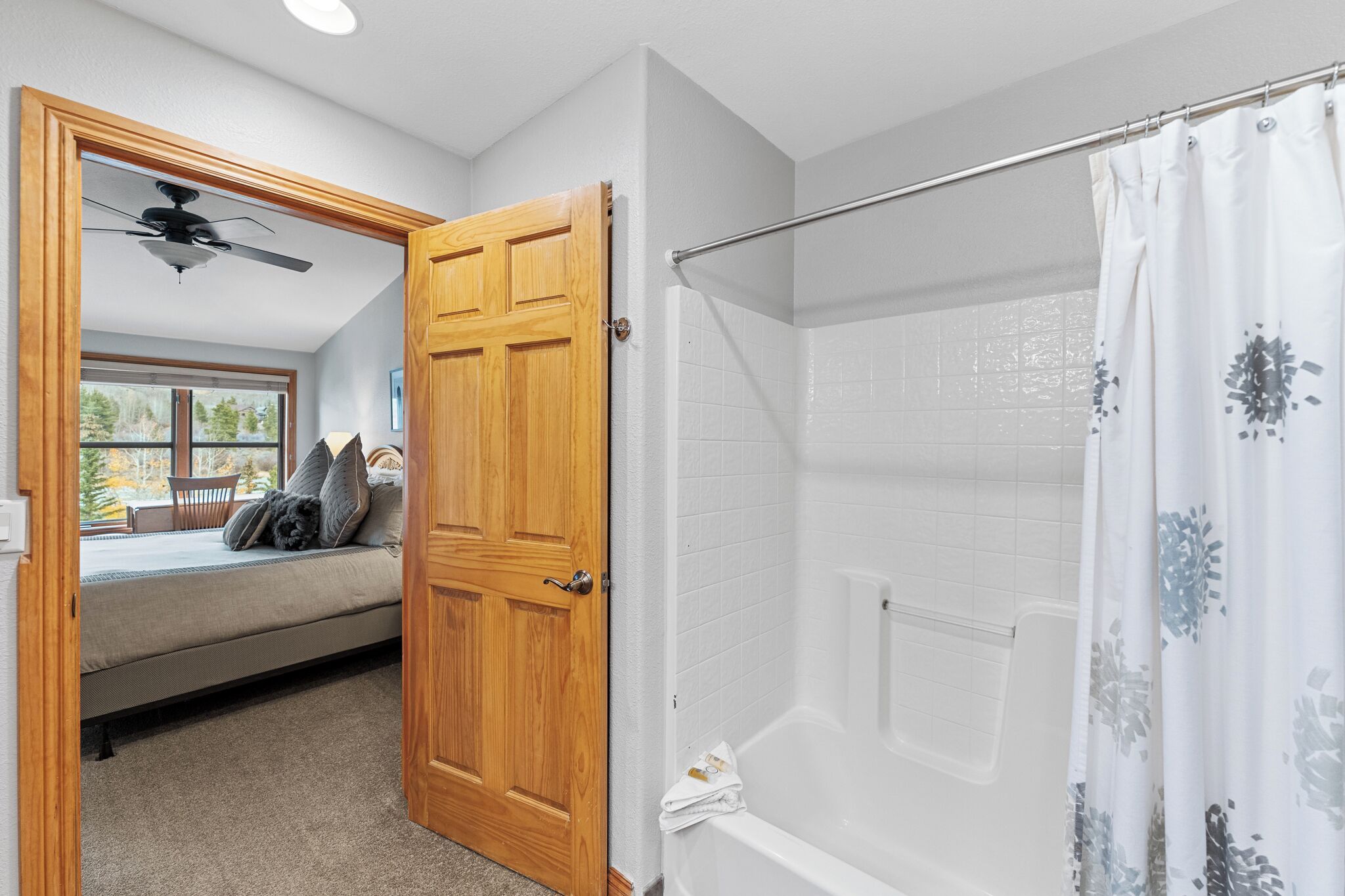 Un dormitorio con una cama, una puerta de madera, un ventanal y un ventilador de techo.