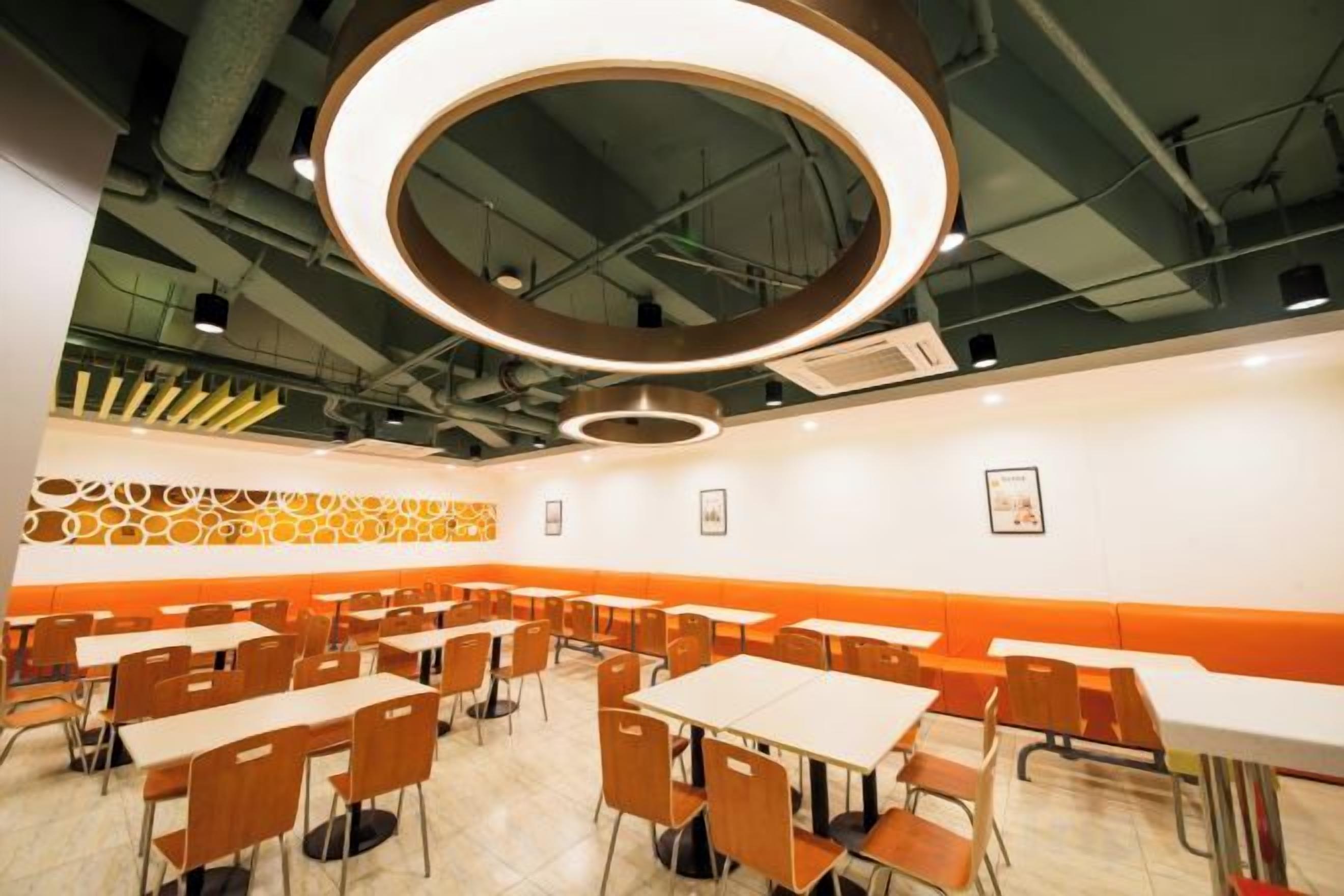 A dining area with multiple tables and chairs, a circular light fixture on the ceiling, and a patterned wall design.