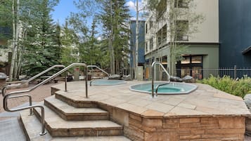 A pool area with steps leading to the pool, surrounded by trees and a building.