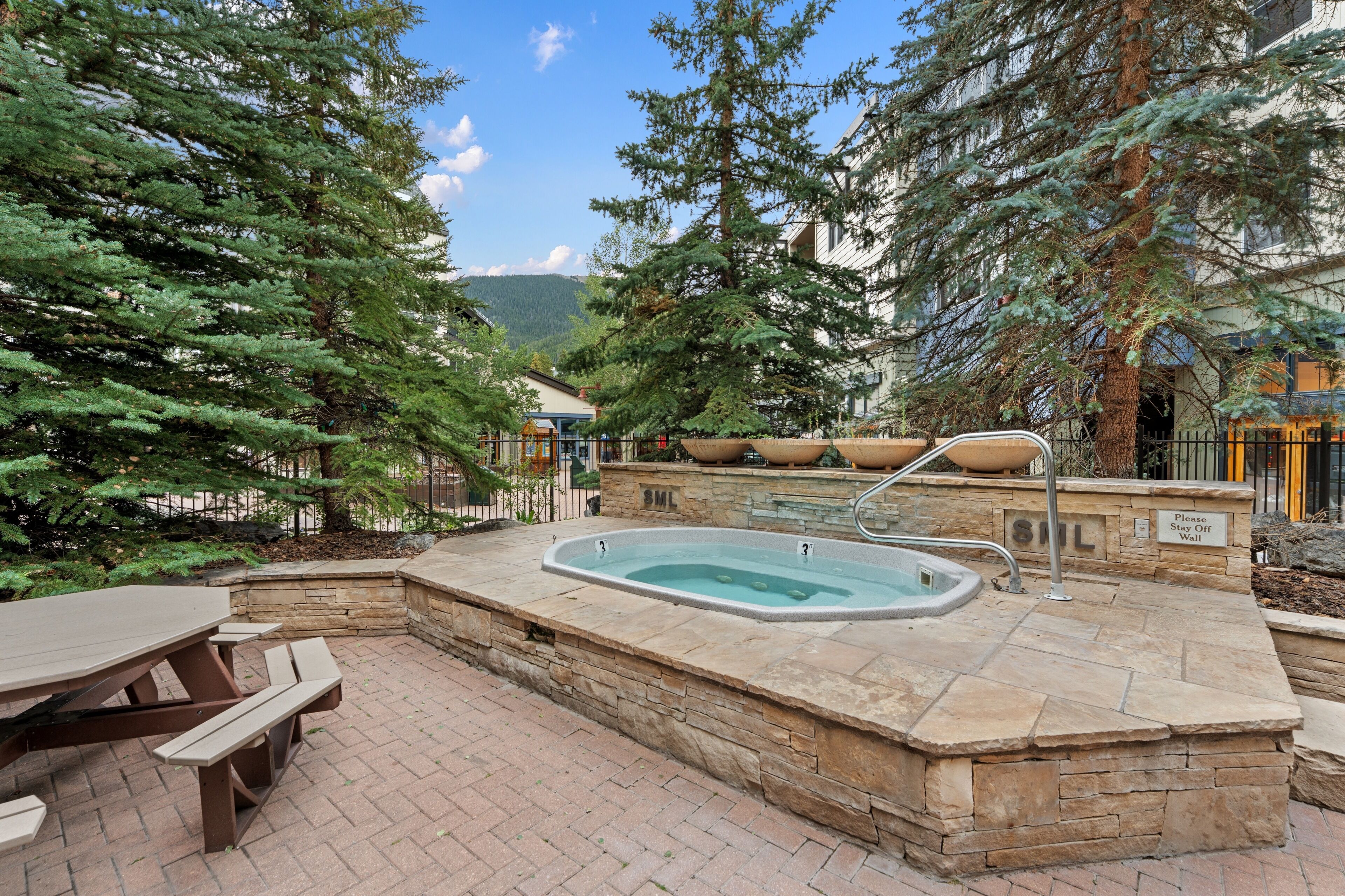 A hot tub surrounded by stone walls, with a picnic table and benches nearby.