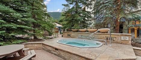 A hot tub surrounded by stone walls, with a picnic table and benches nearby.