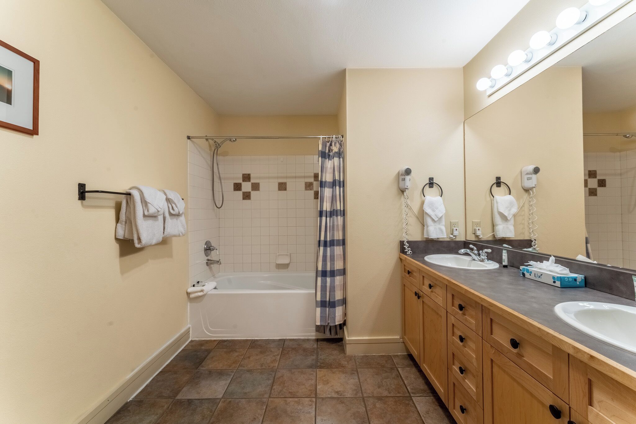 A bathroom with a bathtub, a shower, a vanity with two sinks, and a large mirror with lights.