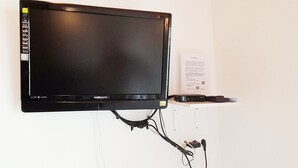 A flat-screen TV mounted on a white wall with a power strip and a small sign.