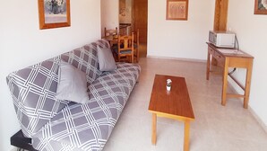 A living room with a patterned sofa, a wooden coffee table, and a television on a wooden stand.