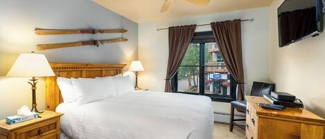 Habitación de hotel con cama, mesitas de noche de madera, escritorio, televisor y esquíes colgados en la pared.