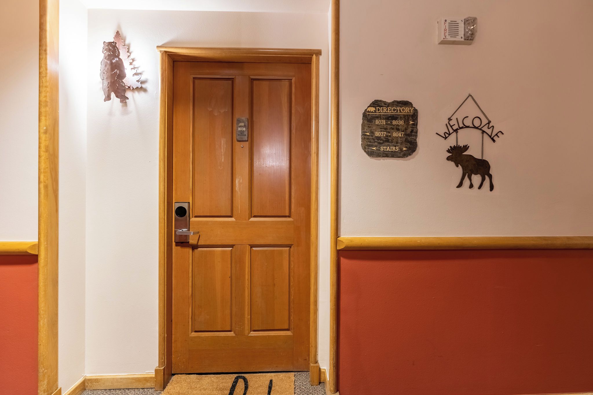 A wooden door with a plaque, a welcome sign with a moose, and a directory sign on the wall.
