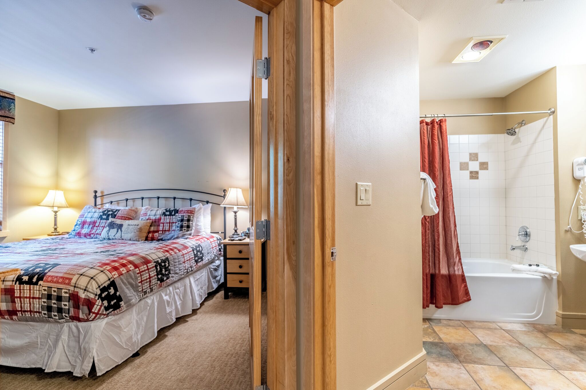A bedroom with a bed, bedside lamps, a nightstand, and a bathroom with a shower, sink, and bathtub.
