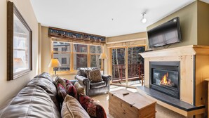 Una sala de estar acogedora con chimenea, sofá de cuero y televisión montada en la pared.
