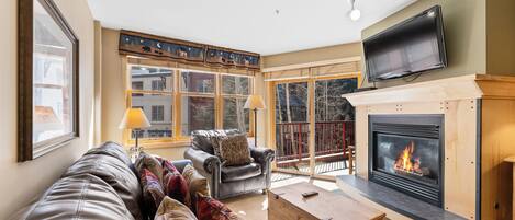 A cozy living room with a fireplace, leather sofa, and a television mounted on the wall.