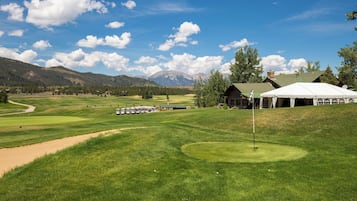 Un campo de golf con una carpa, un edificio y montañas al fondo.