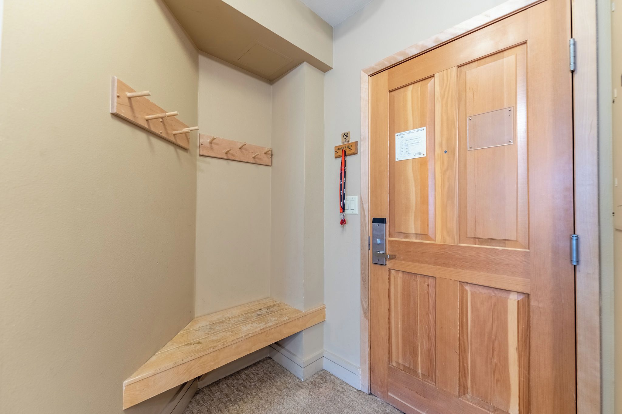 A hallway with a wooden bench, a wooden door with a lock, and a coat rack with a coat hanging.