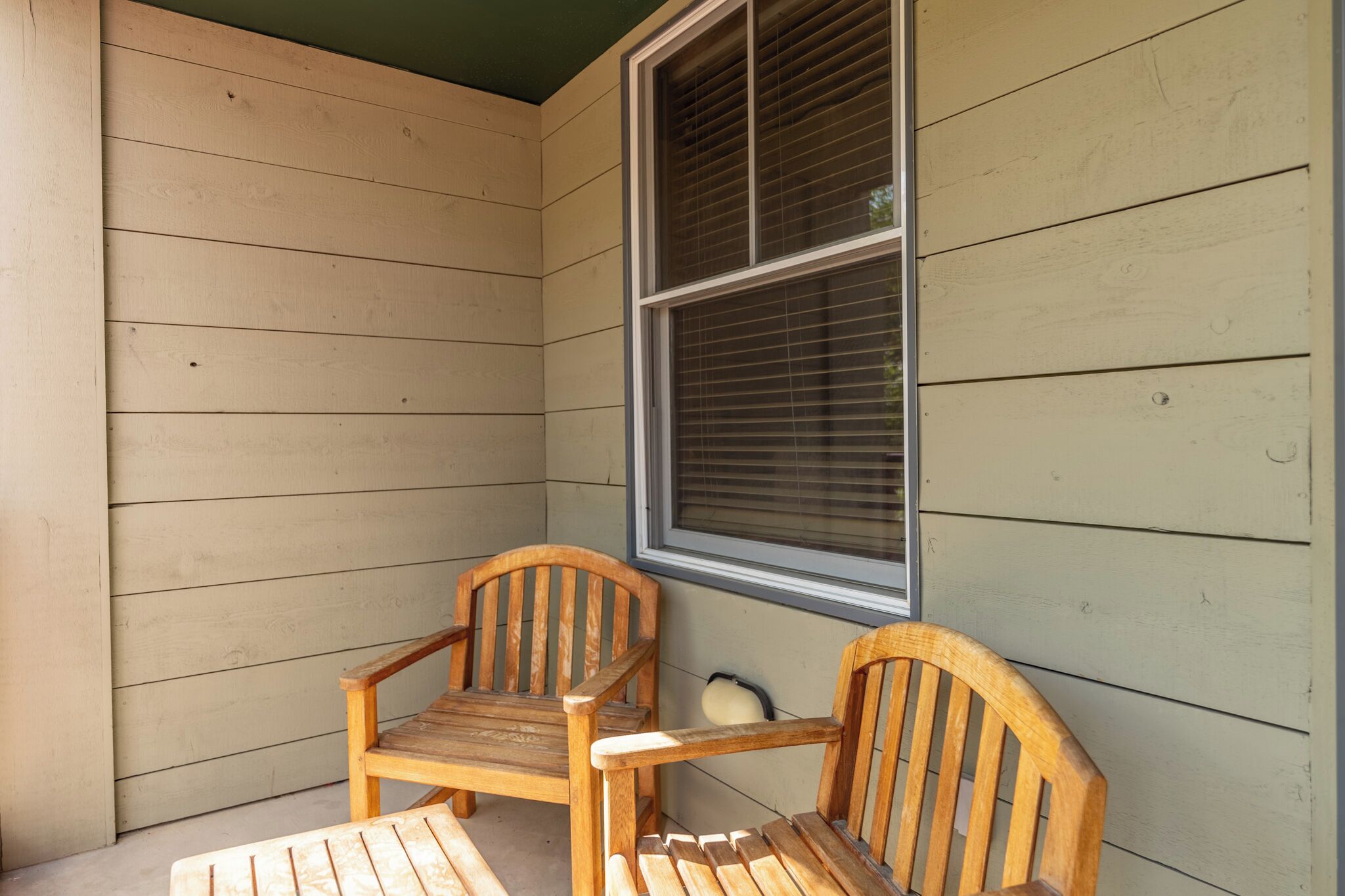 A corner of a room with two wooden chairs and a window with blinds.