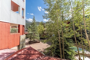 A modern building with a red facade and balconies overlooking a landscaped area with trees and a pool. - Silver Mill #8177 by Summit County Mountain Retreats (Keystone)