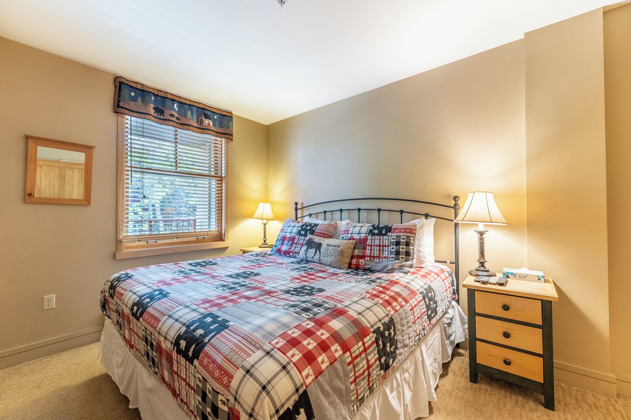 A bedroom with a bed, two bedside lamps, a nightstand, a window with blinds, and a framed picture on the wall.