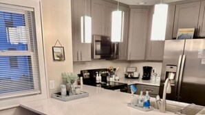 A modern kitchen with a large island, bar stools, stainless steel appliances, and pendant lighting.