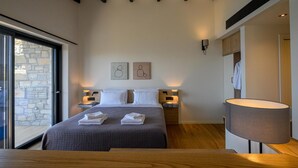A modern bedroom with a large bed, two bedside tables with lamps, a wooden headboard, and a large window with a stone wall view. - Petra Deluxe Studio Suite (West Mani)