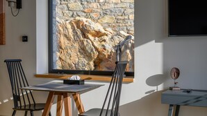 A room with a stone wall, a table with chairs, a TV, and a desk with a lamp. - Petra Deluxe Studio Suite (West Mani)