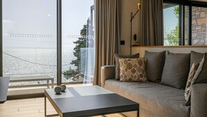 A modern living room with a sofa, a coffee table, and a view of a body of water through large windows. - Petra Deluxe Studio Suite (West Mani)