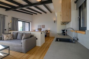 A modern, compact living space with a sofa, a small kitchen area, and a dining table. - Petra Deluxe Studio Suite (West Mani)