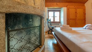 A room with a stone fireplace, wooden ceiling, a bed with white linens, and a wooden wardrobe. - Il Salice by Wonderful Italy (Bellagio)