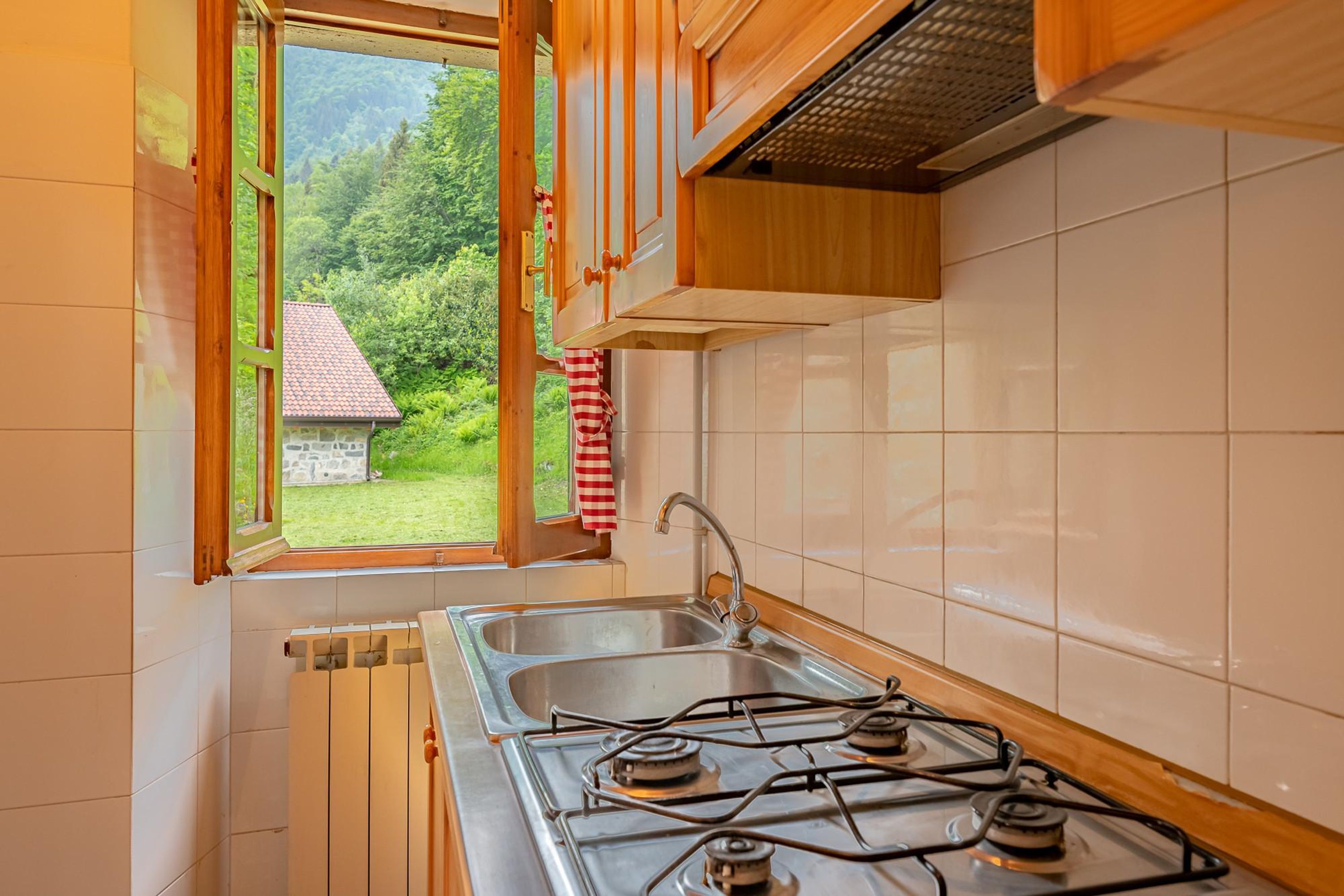 A kitchen with a gas stove, a sink, and a window overlooking a garden.
