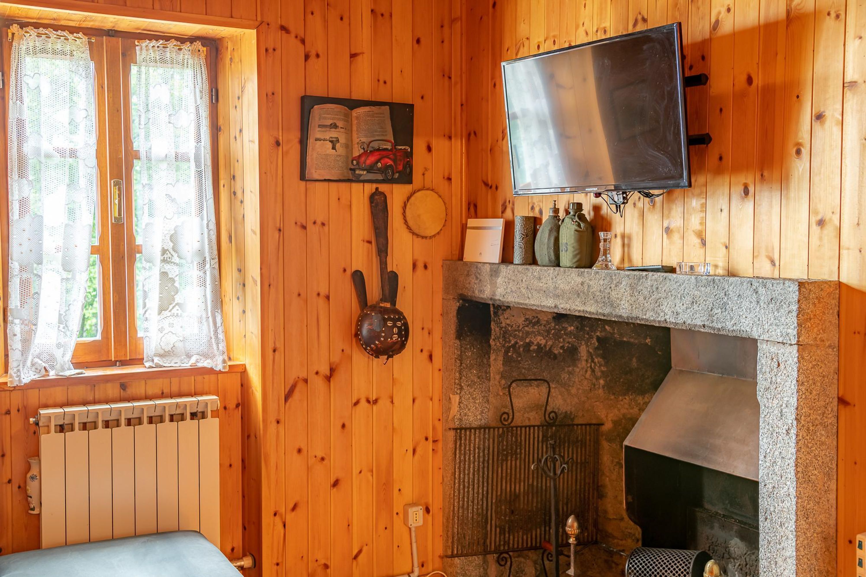 A cozy room with wooden walls, a fireplace, a television, and a window with lace curtains.