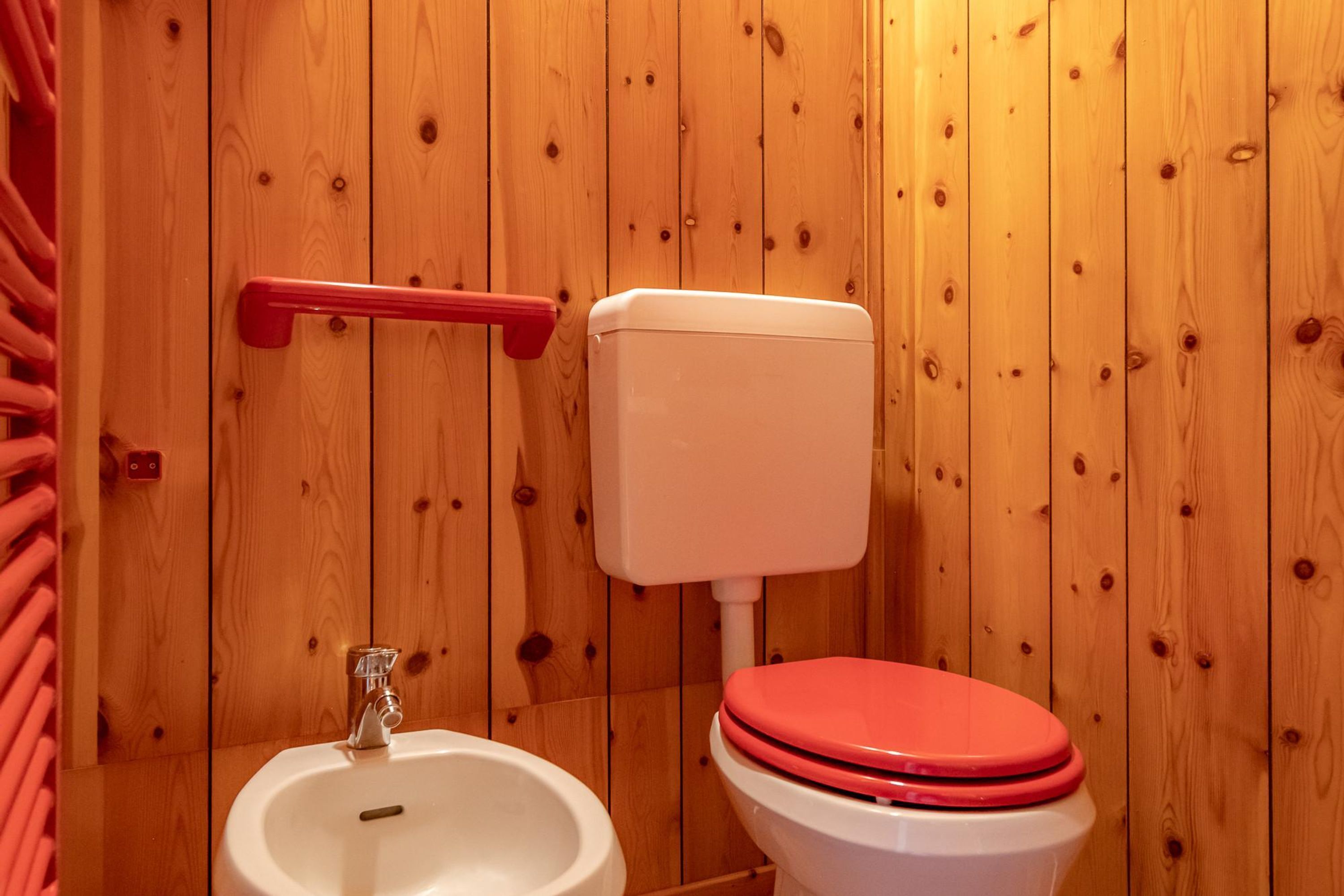 A wooden-paneled bathroom with a white sink, a red toilet, and a red towel rack.