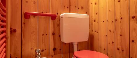 A wooden-paneled bathroom with a white sink, a red toilet, and a red towel rack.