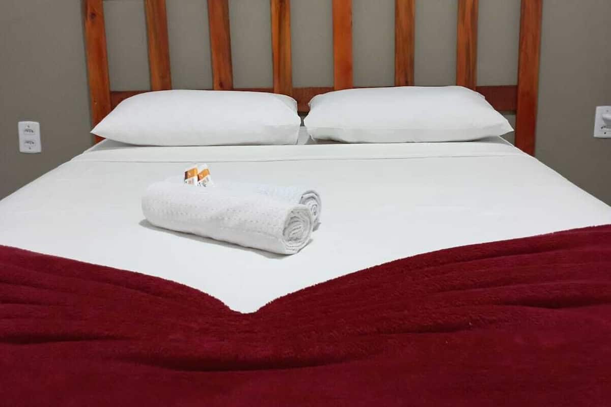 Una cama bien hecha con sábanas blancas, dos almohadas y una toalla blanca enrollada.