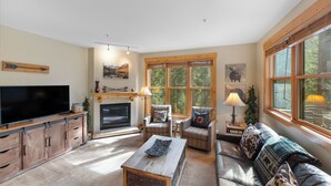 A cozy living room with a fireplace, comfortable seating, and large windows offering a view of the outdoors. - Trapper's Crossing #8768 by Summit County Mountain Retreats  (Keystone)