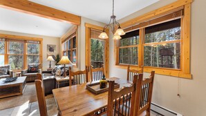 A wooden dining table with chairs, a lamp, and a window with a view of trees. - Trapper's Crossing #8768 by Summit County Mountain Retreats  (Keystone)
