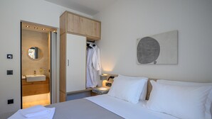 Une chambre d’hôtel comprenant un lit, une table de chevet, une commode, une armoire, une salle de bain avec un lavabo et un miroir.