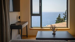 Une pièce comprenant un bureau, une chaise, une petite table agrémentée d’un objet décoratif et une grande fenêtre donnant sur la mer.