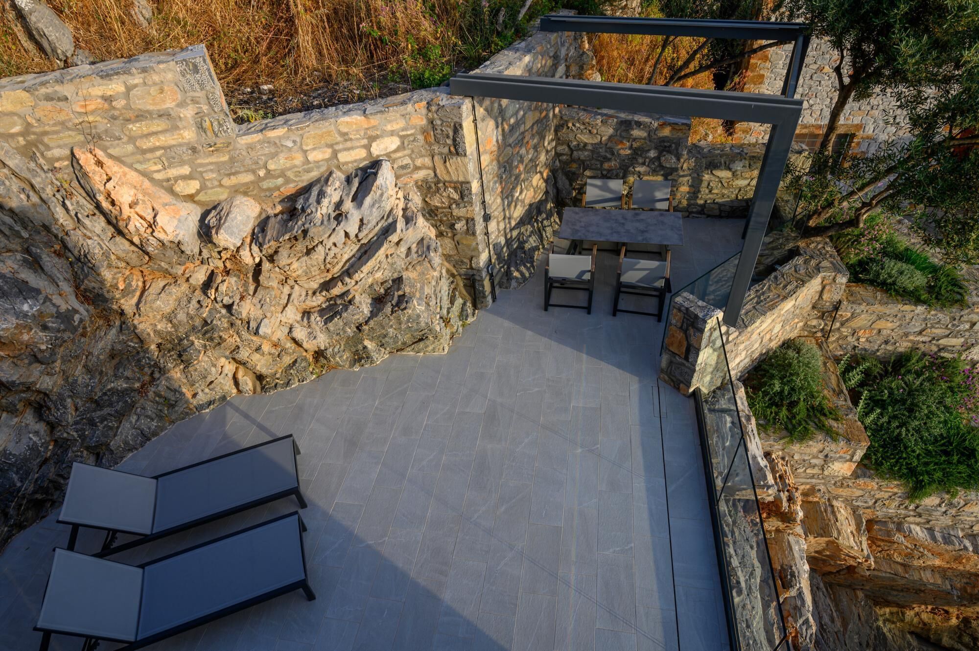 A stone-walled outdoor patio with a table and chairs, surrounded by natural rock formations.