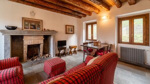 A cozy room with a fireplace, wooden beams, a dining area, and a large window. - Il Faggio by Wonderful Italy (Bellagio)