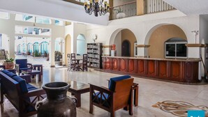 A spacious lobby with a high ceiling, a chandelier, seating areas, a fireplace, and a view of the outdoor courtyard. - Tiara Sands condo excelente ubicación (Mazatlán)