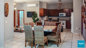 A modern kitchen with wooden cabinets, a microwave, and a dining area with patterned chairs and a central table. - Tiara Sands condo excelente ubicación (Mazatlán)