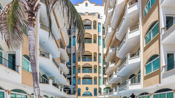 A multi-story hotel with balconies, a central pool, and palm trees. - Tiara Sands condo excelente ubicación (Mazatlán)