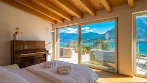 A bedroom with a piano, a bed with towels, a balcony with wicker furniture, and a scenic mountain view. - Villa Bianca (San Felice del Benaco)